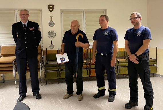 Immer gut behütet mit dem Schirm des Kreis&shy;feuerwehr&shy;verbandes, den es zur Auszeichnung mit dazu gab. Überbracht vom Vorstand für Jugendarebeit Stefan Kothe. (links) Wehrführer Rico Nowka und sein Stellvertreter Nico Hammel gratulieren.