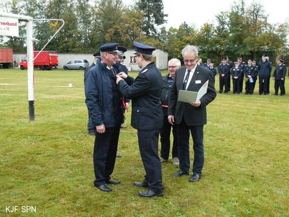 Kreis&shy;jugend&shy;feuerwehrwart Christian Rösiger übergibt Bernd Schulze das Ehrenzeichen der Landesjugendfeuerwehr Brandenburg in Bronze aus.