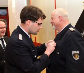 Vorsitzender des Kreis&shy;feuerwehr&shy;verbandes Spree-Neiß e.V. Robert Buder steckt dem ausgezeichneten Carsten Brudek das Abzeichen an die Uniformjacke.