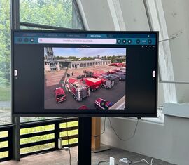 Wipfel-BRAND 2025, Samstag, Monitor im Hanger bei der Verpfelung der Brandschutzeinheiten mit Live Bildern der Übung